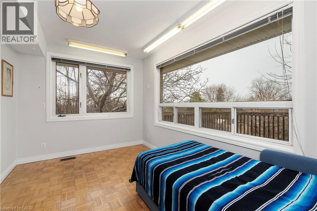This room features parquet flooring, a large window providing ample natural light, and a second expansive window with views of trees and a wooden railing - 36 Buckingham Drive, Hamilton, ON - Indoor