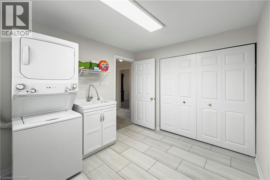 Well-appointed laundry area featuring a stacked washer and dryer, a utility sink with white cabinetry, and extensive built-in storage with bi-fold doors - 36 Buckingham Drive, Hamilton, ON - Indoor Photo Showing Laundry Room