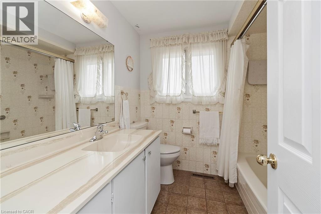 This bathroom features a lengthy vanity with an integrated sink, a large mirror, a toilet, and a bathtub with a shower - 36 Buckingham Drive, Hamilton, ON - Indoor Photo Showing Bathroom