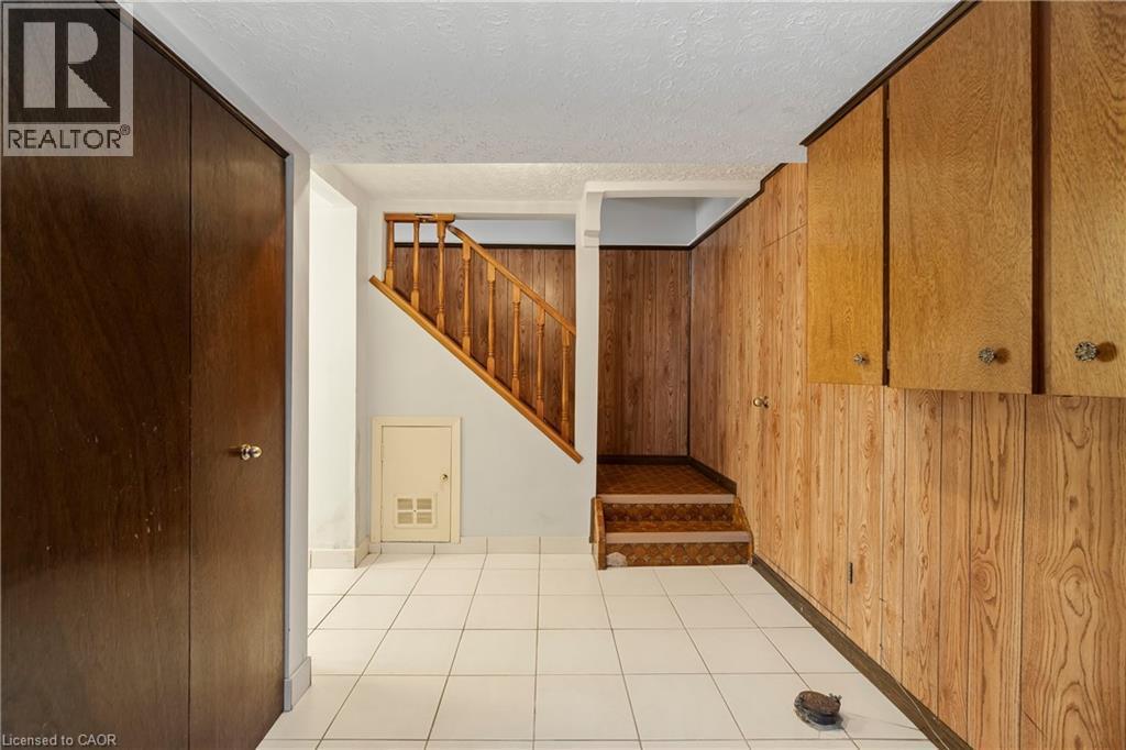 This area features white tiled flooring, wood paneling on the walls, and a wooden staircase with a banister - 36 Buckingham Drive, Hamilton, ON - Indoor Photo Showing Other Room