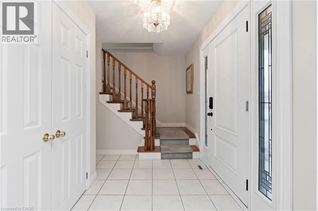 Bright entryway featuring white tiled flooring, a clear crystal chandelier, and a staircase with wooden handrails and carpeted treads - 36 Buckingham Drive, Hamilton, ON - Indoor Photo Showing Other Room
