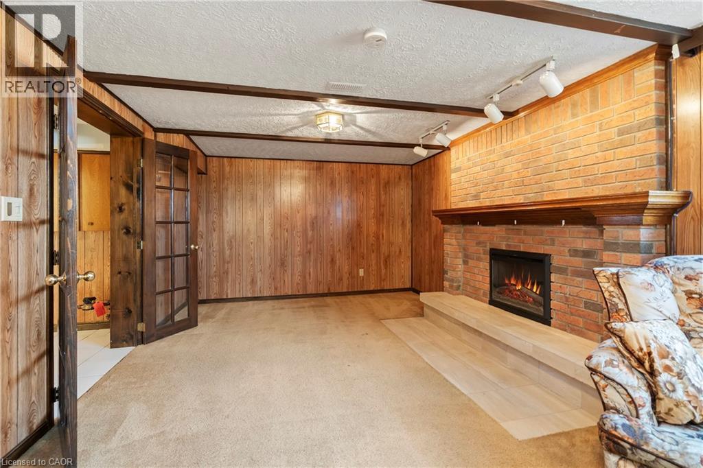Living area featuring wood paneling, a brick fireplace with a wood mantle, and a carpeted floor - 36 Buckingham Drive, Hamilton, ON - Indoor With Fireplace