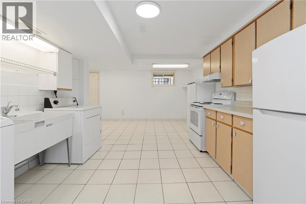 This functional utility space features a combination of laundry and kitchen amenities, including a utility sink, washing machine, dryer, refrigerator, range, and various cabinetry - 36 Buckingham Drive, Hamilton, ON - Indoor Photo Showing Laundry Room