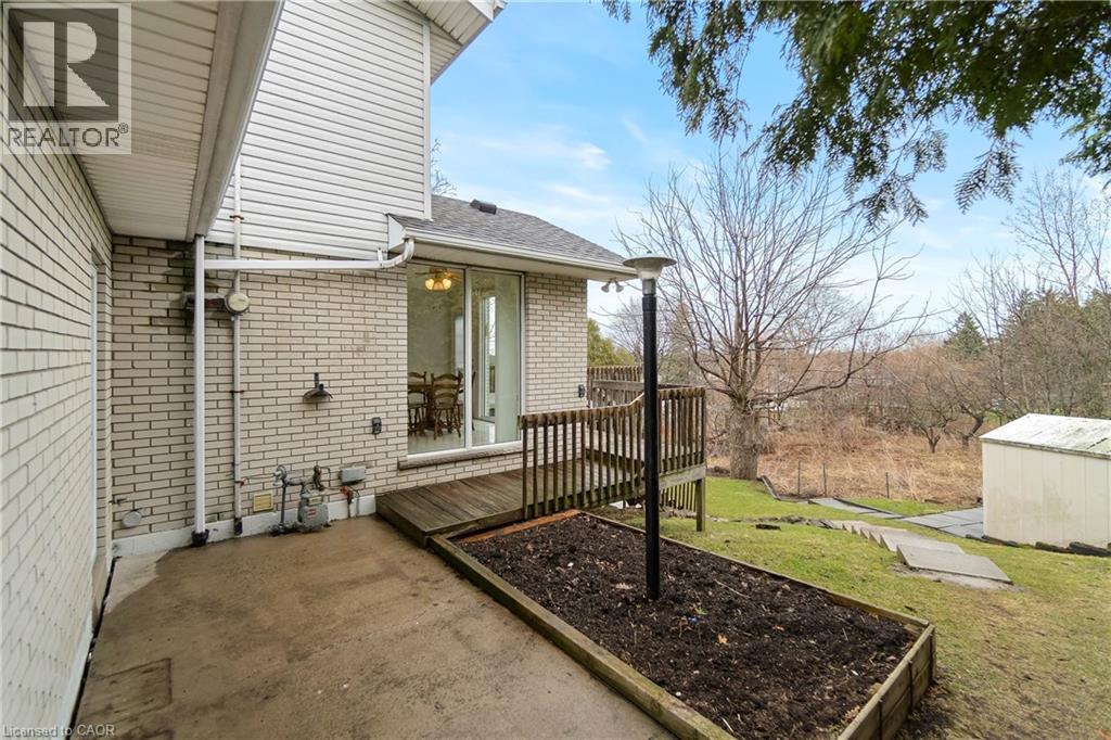 This property features an exterior with light-colored brick siding and white vinyl siding, a wooden deck with railing, and a concrete patio area - 36 Buckingham Drive, Hamilton, ON - Outdoor With Exterior
