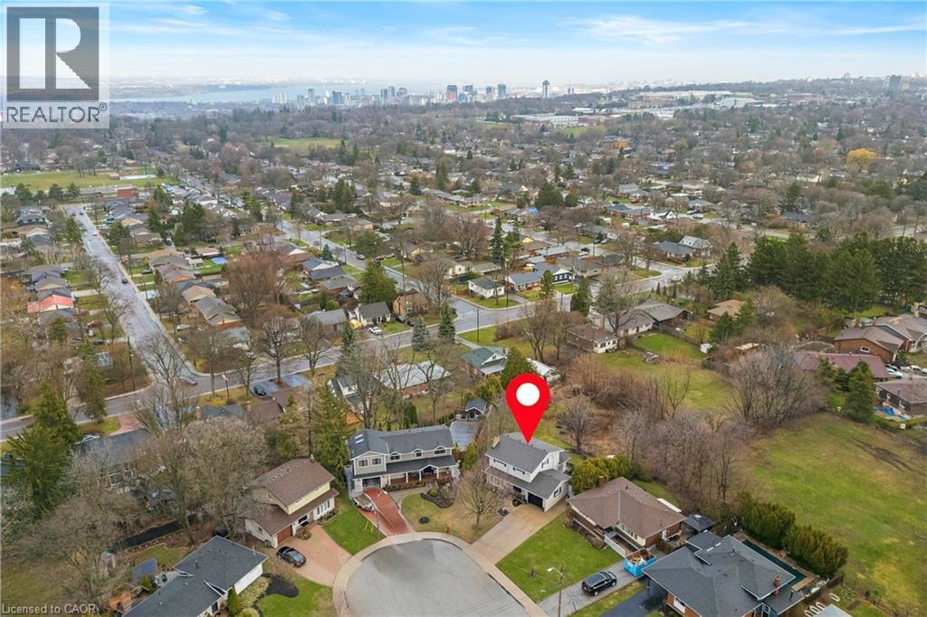 Aerial view of the property and its surrounding residential neighborhood, featuring established trees and a distant cityscape under a blue sky - 36 Buckingham Drive, Hamilton, ON - Outdoor With View
