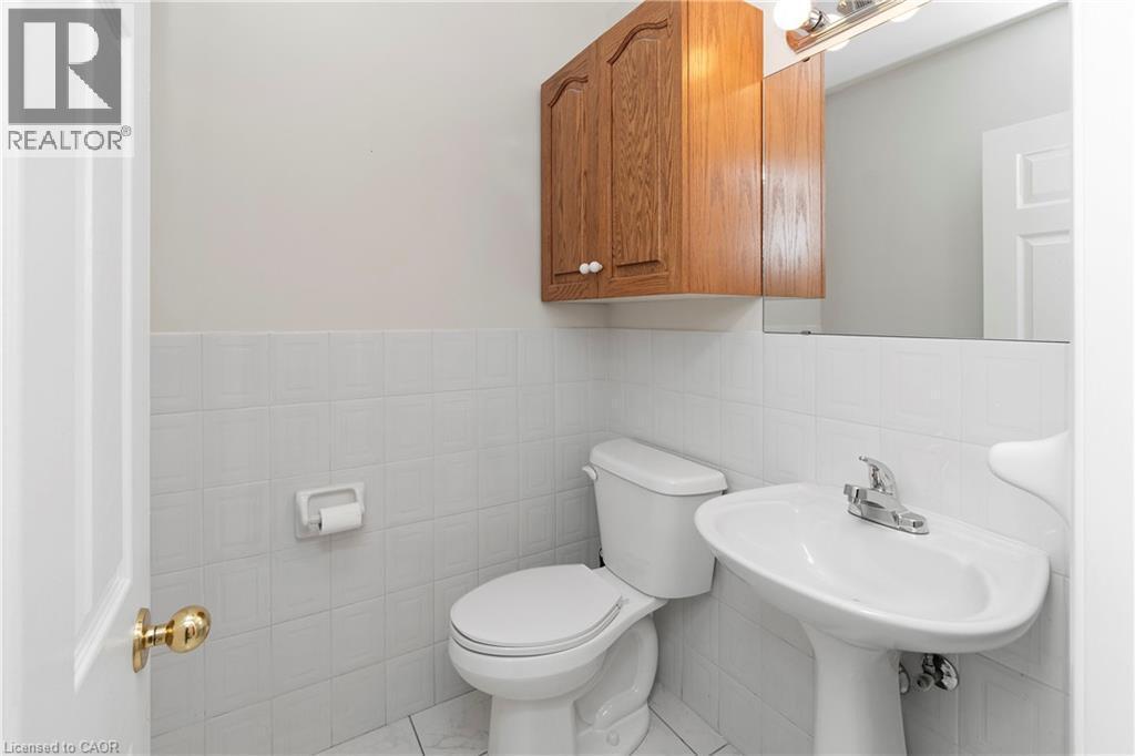 Bathroom featuring a pedestal sink, a toilet, a wooden wall cabinet, and a wall-mounted mirror with a light fixture - 36 Buckingham Drive, Hamilton, ON - Indoor Photo Showing Bathroom
