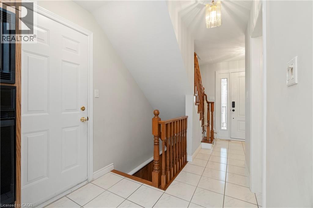 The property features a bright entrance hall with white tiled flooring, a wooden staircase, and a decorative overhead light fixture - 36 Buckingham Drive, Hamilton, ON - Indoor Photo Showing Other Room