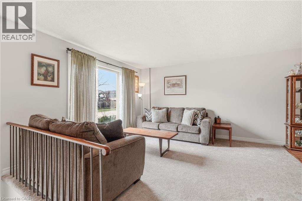 Living area featuring light-colored carpet flooring, light-toned walls, and a large window with sheer drapes providing natural light - 2349 Middlesmoor Crescent, Burlington, ON - Indoor Photo Showing Living Room