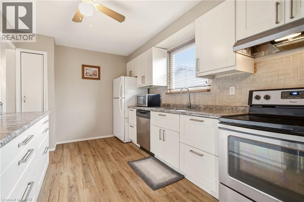 The kitchen features wood-look flooring, white cabinetry with silver hardware, and a window with horizontal blinds - 2349 Middlesmoor Crescent, Burlington, ON - Indoor Photo Showing Kitchen