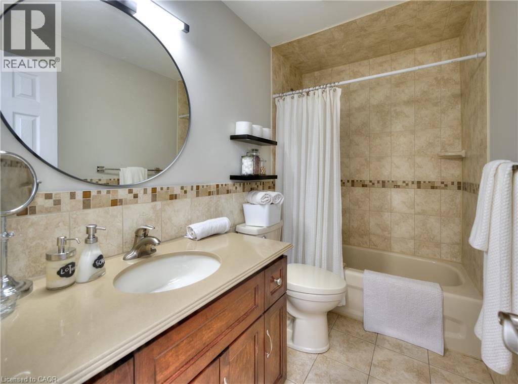 Bathroom featuring a vanity with a light-colored countertop, a round mirror, and a bathtub with tiled walls - 42 Culpepper Drive, Waterloo, ON - Indoor Photo Showing Bathroom
