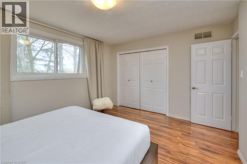 The bedroom features hardwood floors, a window with views of trees, and two sets of bi-fold closet doors - 42 Culpepper Drive, Waterloo, ON - Indoor Photo Showing Bedroom