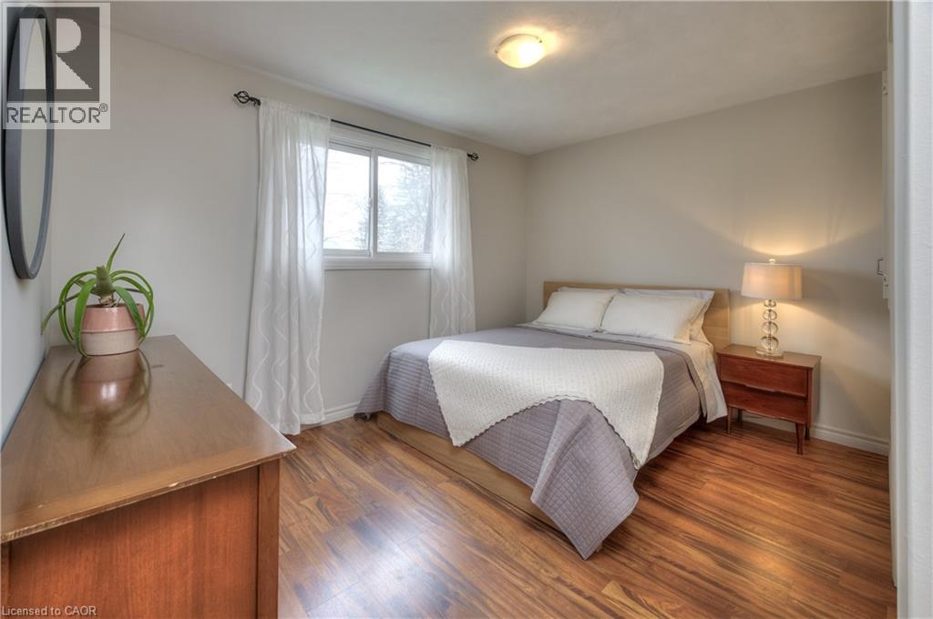 This room features warm hardwood flooring, a window with sheer curtains, and a ceiling-mounted light fixture - 42 Culpepper Drive, Waterloo, ON - Indoor Photo Showing Bedroom