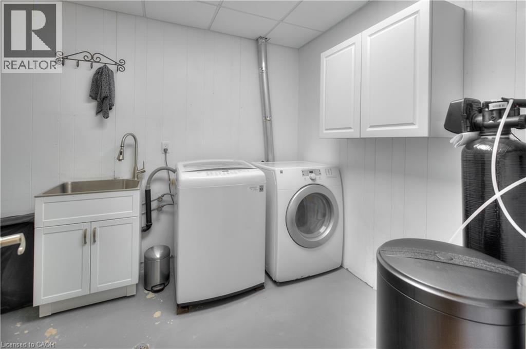 This utility area features white paneled walls, a stainless steel sink with a modern faucet, and white cabinetry - 42 Culpepper Drive, Waterloo, ON - Indoor Photo Showing Laundry Room