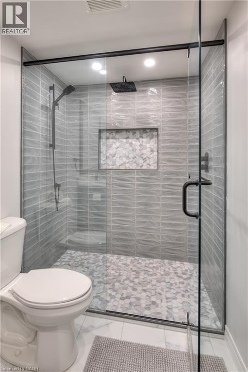 The bathroom features a spacious shower with glass enclosure, textured tile walls, a built-in shower niche, and a contrasting tile floor - 42 Culpepper Drive, Waterloo, ON - Indoor Photo Showing Bathroom