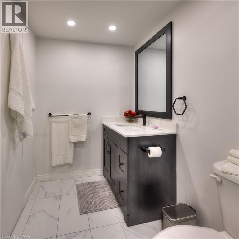 Bathroom featuring a dark wood vanity with a white countertop and sink, a large mirror with a dark frame, and white tiled flooring - 42 Culpepper Drive, Waterloo, ON - Indoor Photo Showing Bathroom