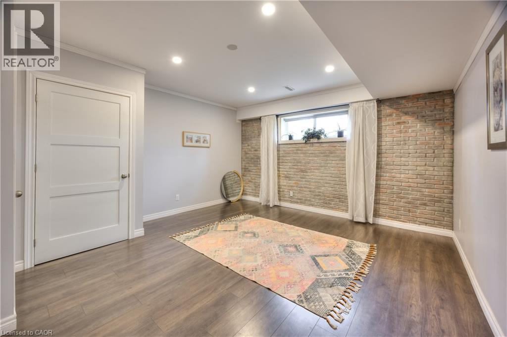 Living area featuring a modern wood-look floor, recessed lighting, and an exposed brick accent wall - 42 Culpepper Drive, Waterloo, ON - Indoor Photo Showing Other Room