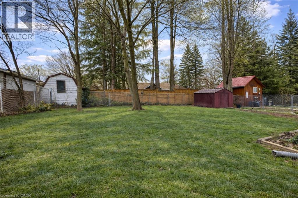The property offers a spacious yard with a lush lawn, established trees, and a wooden fence - 42 Culpepper Drive, Waterloo, ON - Outdoor