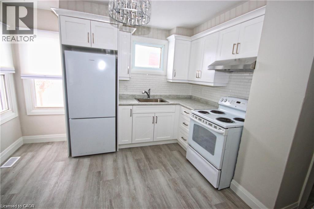 The kitchen features white cabinetry, light-colored countertops, a white refrigerator, and a white electric range with a stainless steel hood fan - 1356 Upper Wellington Street, Hamilton, ON - Indoor Photo Showing Kitchen