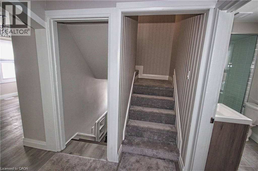 The property features a staircase with carpeted steps and striped wallpaper, a bathroom with a glass-enclosed shower, and a vanity with a white countertop - 1356 Upper Wellington Street, Hamilton, ON - Indoor Photo Showing Other Room