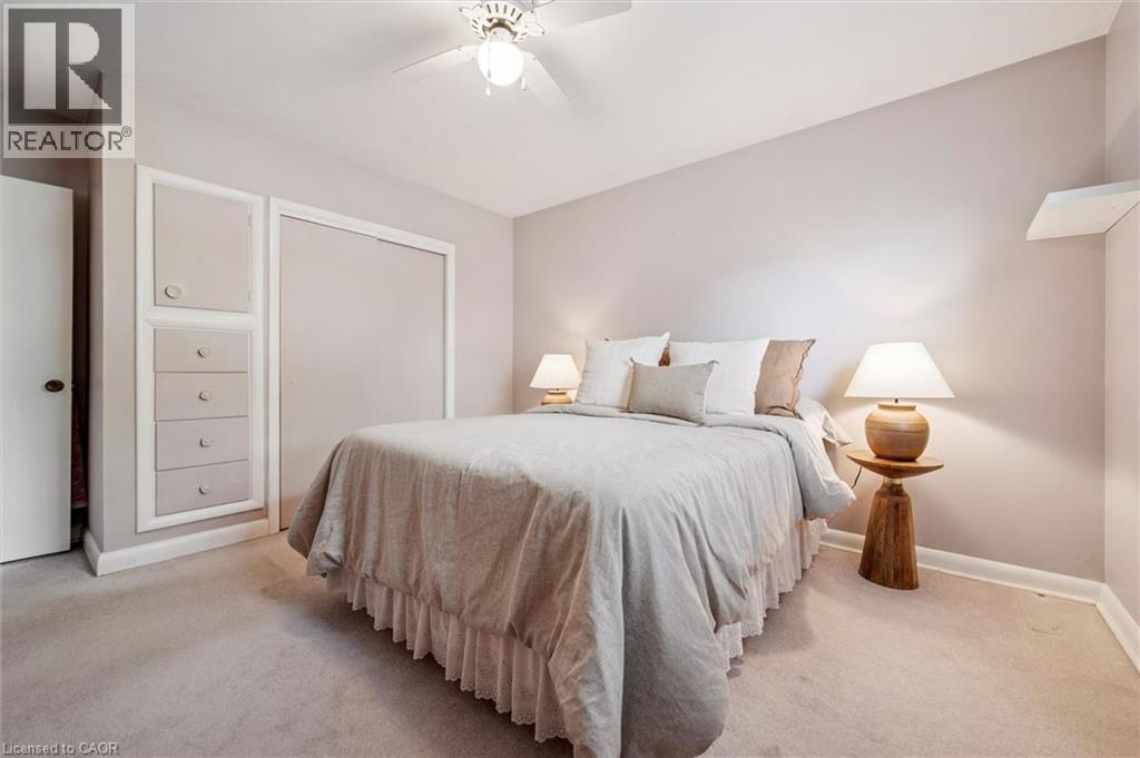 This room features light-colored walls and carpeting, a ceiling fan, a built-in storage unit with drawers, and a closet with sliding doors - 155 Hungerford Road, Cambridge, ON - Indoor Photo Showing Bedroom