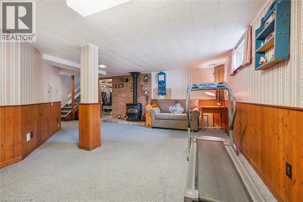 This versatile room features carpeted flooring, wood paneling, and a brick fireplace - 155 Hungerford Road, Cambridge, ON - Indoor