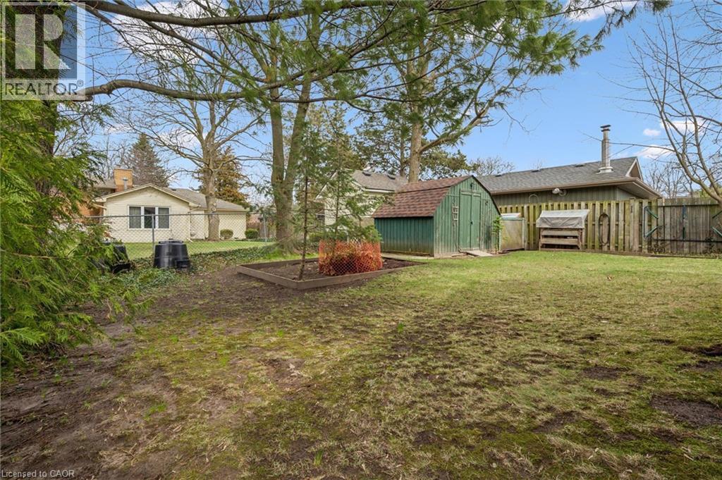 The property features a spacious yard with a green storage shed, a wooden fence, and mature trees - 155 Hungerford Road, Cambridge, ON - Outdoor