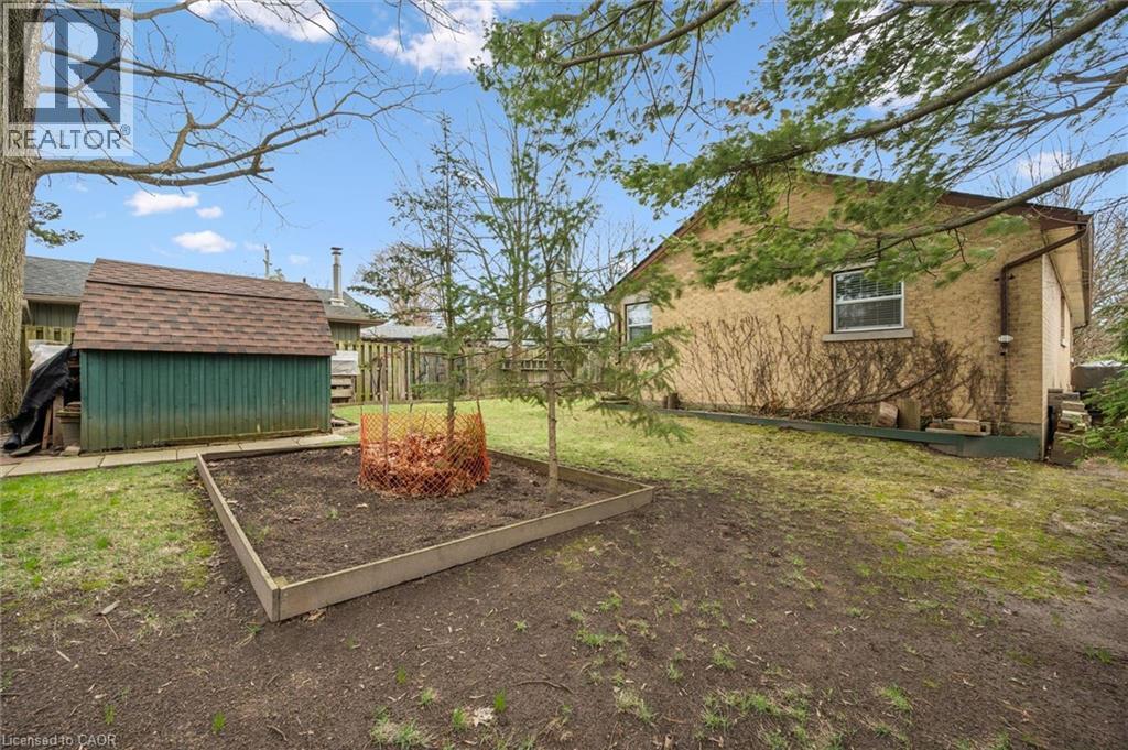 The property includes an exterior storage shed with a shingled roof, a raised garden bed, and a spacious yard with mature trees - 155 Hungerford Road, Cambridge, ON - Outdoor