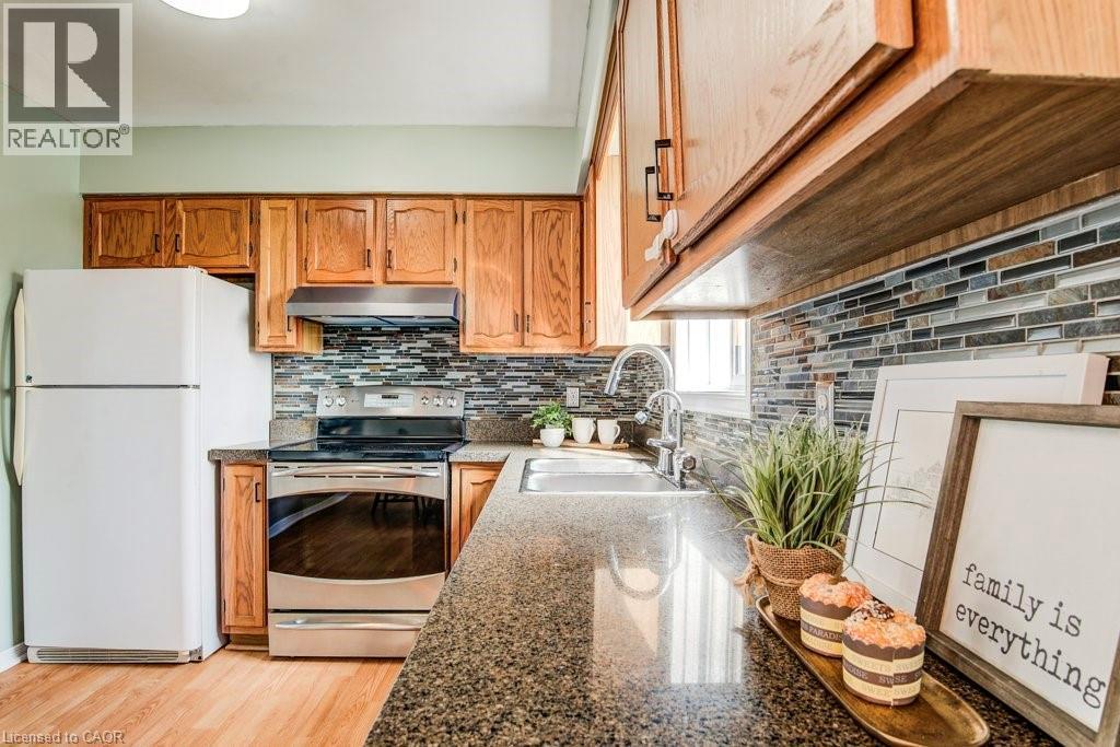 Kitchen featuring stainless steel electric stove, dark stone counters, freestanding refrigerator, tasteful backsplash, and wood finish cabinetry - 633 Grange Crescent, Waterloo, ON - Indoor Photo Showing Kitchen
