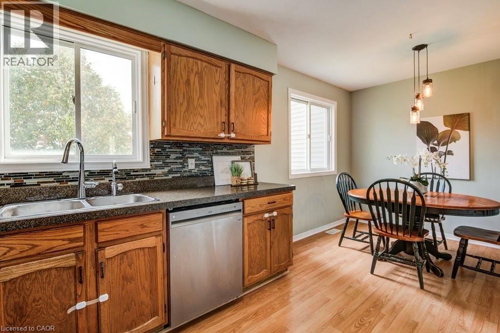 Kitchen with dark countertops, stainless steel dishwasher, wood finish cabinetry, light wood finished floors, and decorative light fixtures - 633 Grange Crescent, Waterloo, ON - Indoor Photo Showing Kitchen With Double Sink