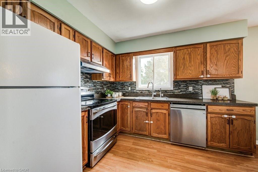 Kitchen featuring stainless steel appliances, light wood-style flooring, wood finish cabinetry, and decorative backsplash - 633 Grange Crescent, Waterloo, ON - Indoor Photo Showing Kitchen