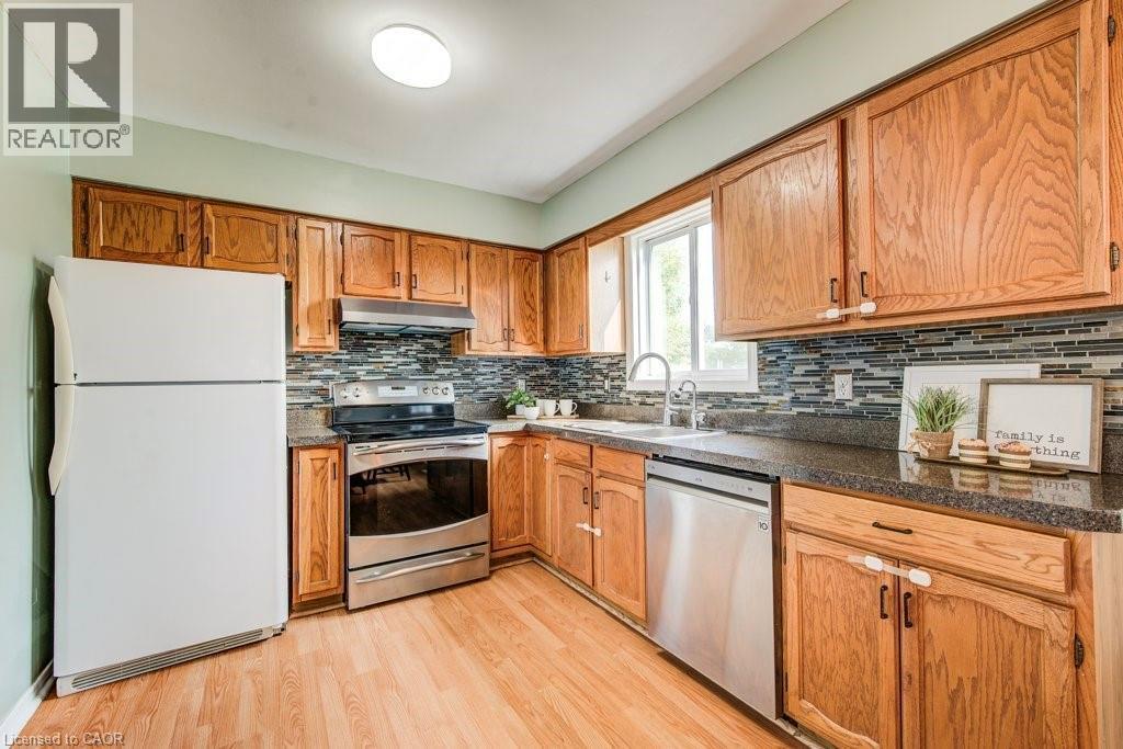 Kitchen with stainless steel appliances, light wood-style flooring, wood finish cabinetry, dark stone countertops, and tasteful backsplash - 633 Grange Crescent, Waterloo, ON - Indoor Photo Showing Kitchen