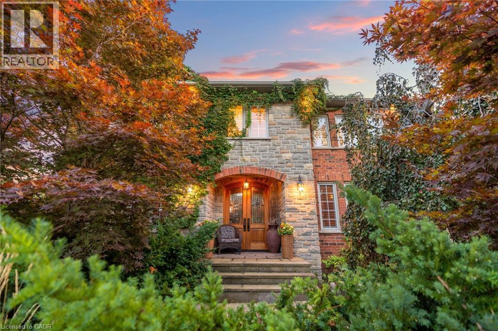 The property features a stone and brick exterior, with mature trees and extensive landscaping surrounding the entrance - 4278 Clubview Drive, Burlington, ON - Outdoor With Deck Patio Veranda