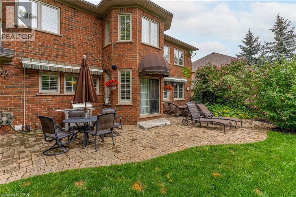 This property features an expansive brick exterior with numerous windows, complemented by a paver patio and a lush green lawn - 4278 Clubview Drive, Burlington, ON - Outdoor With Deck Patio Veranda
