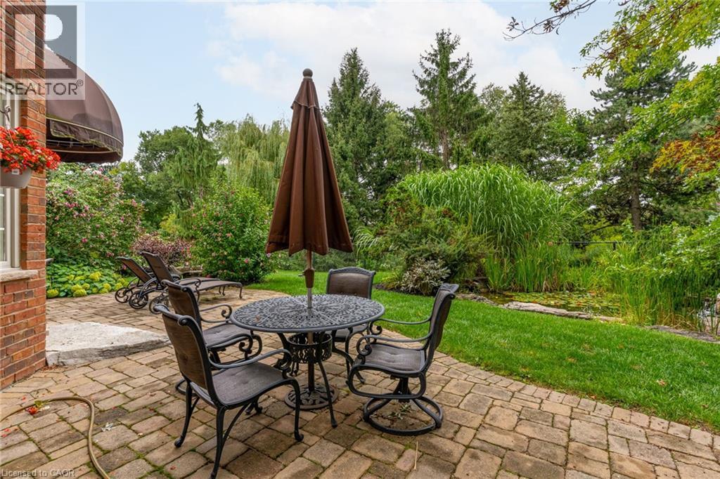 The property features a spacious paver patio, a lush lawn, and mature trees, creating a serene outdoor environment - 4278 Clubview Drive, Burlington, ON - Outdoor With Deck Patio Veranda