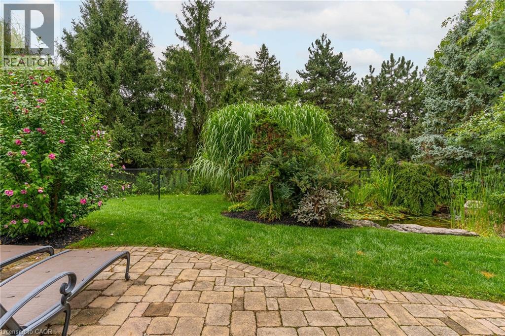 The property features an extensive yard with a paved patio, a lush lawn, and mature trees - 4278 Clubview Drive, Burlington, ON - Outdoor