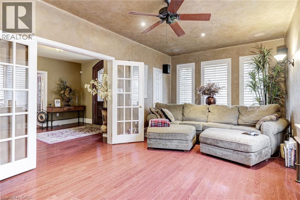 Living space featuring polished hardwood floors, a ceiling fan, and three windows with white louvered blinds - 4278 Clubview Drive, Burlington, ON - Indoor Photo Showing Living Room
