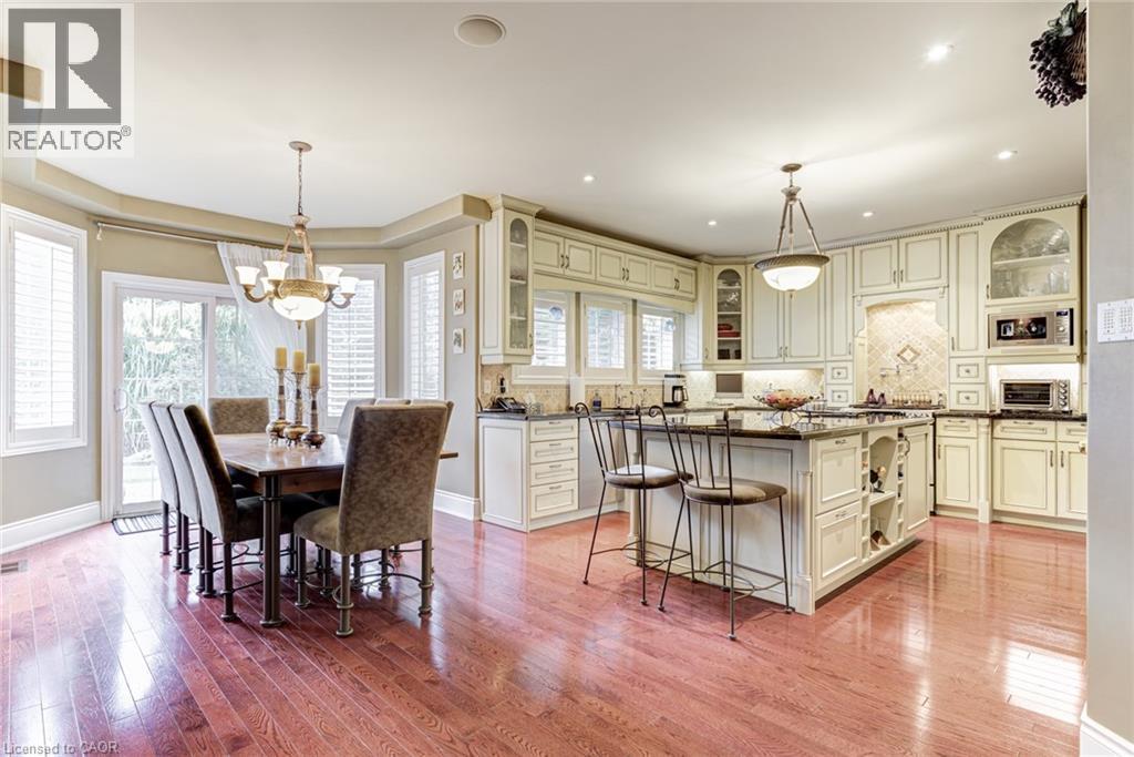 An open-concept kitchen and dining area featuring hardwood floors, cream cabinetry, a kitchen island with seating, and a dining area with large windows and a glass sliding door - 4278 Clubview Drive, Burlington, ON - Indoor Photo Showing Dining Room