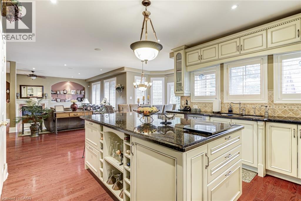 The kitchen features a large island with a dark granite countertop, light-colored cabinetry with decorative molding, and a tiled backsplash - 4278 Clubview Drive, Burlington, ON - Indoor Photo Showing Kitchen With Upgraded Kitchen