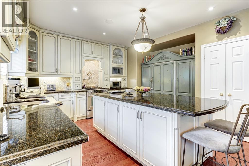 The kitchen features an expansive island with a dark granite countertop, white cabinetry, and hardwood flooring - 4278 Clubview Drive, Burlington, ON - Indoor Photo Showing Kitchen