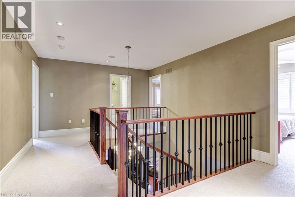 Spacious landing area featuring neutral-toned walls, recessed lighting, and a chandelier, with carpeted flooring and a staircase with a dark wood handrail and black spindles - 4278 Clubview Drive, Burlington, ON - Indoor Photo Showing Other Room