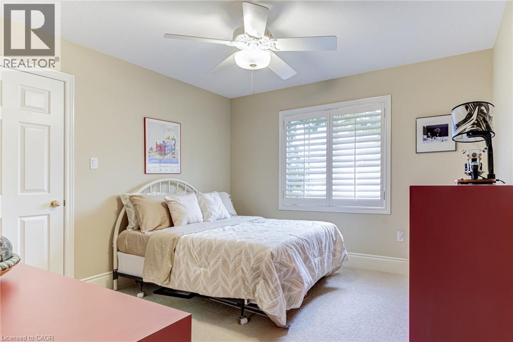 Bedroom featuring light-colored walls, carpeted flooring, a window with white louvered shutters, and a ceiling fan with an integrated light fixture - 4278 Clubview Drive, Burlington, ON - Indoor Photo Showing Bedroom