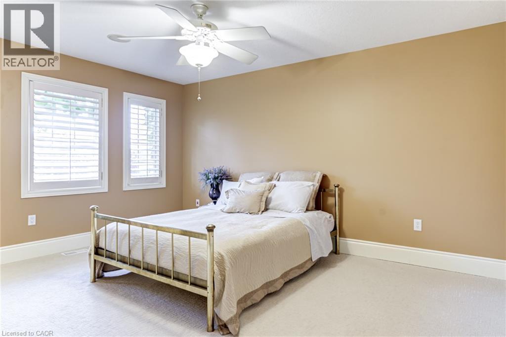 Bedroom featuring two windows with white louvered shutters, a ceiling fan with integrated lighting, and light-colored carpeting - 4278 Clubview Drive, Burlington, ON - Indoor Photo Showing Bedroom