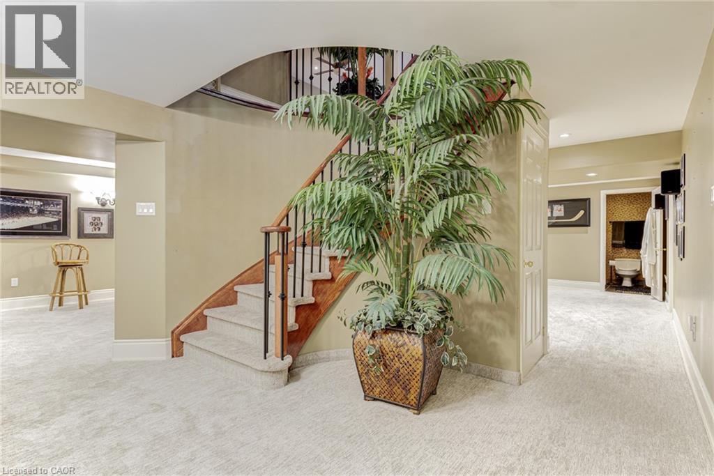 Well-lit interior space featuring light-colored carpeting, a curved wooden staircase with dark balusters, and warm-toned walls - 4278 Clubview Drive, Burlington, ON - Indoor Photo Showing Other Room
