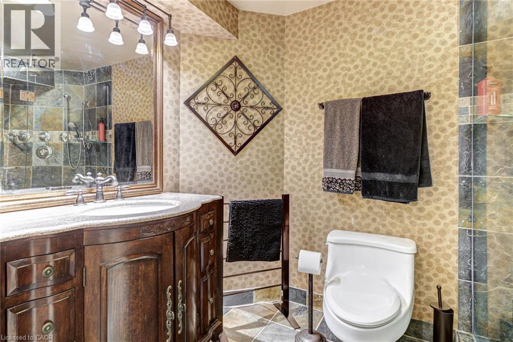 Bathroom featuring a dark wood vanity with a white countertop and basin sink, a large framed mirror, and a shower with tiled walls - 4278 Clubview Drive, Burlington, ON - Indoor Photo Showing Bathroom