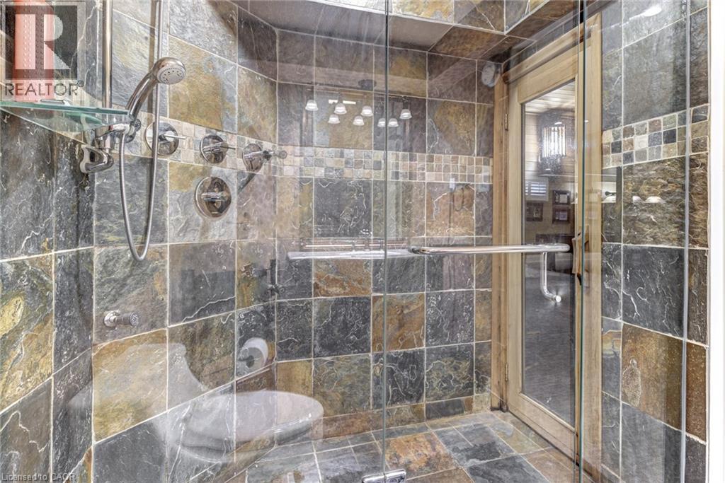 This shower features stone tile walls and flooring, a glass enclosure, and a handheld showerhead - 4278 Clubview Drive, Burlington, ON - Indoor Photo Showing Bathroom