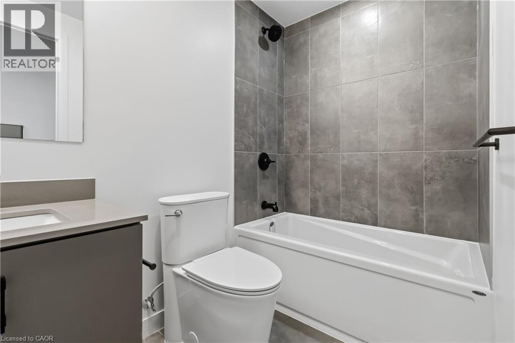Bathroom featuring a white bathtub with dark fixtures, a toilet, and a vanity with a rectangular sink and mirror - 4878 Powers Common Unit# 224, Burlington, ON - Indoor Photo Showing Bathroom