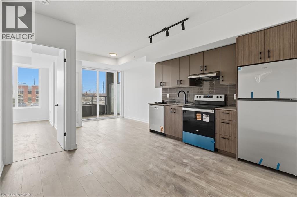 Open concept living area featuring light-toned flooring, a modern kitchen with integrated appliances, and a sliding glass door leading to a balcony - 4878 Powers Common Unit# 224, Burlington, ON - Indoor Photo Showing Kitchen