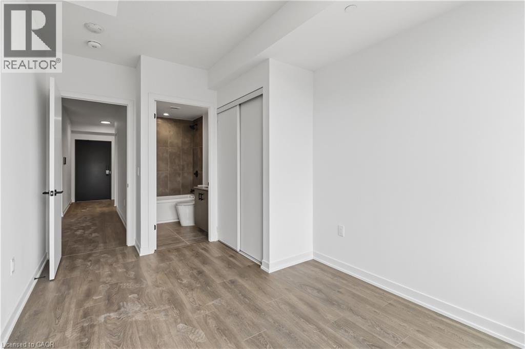This room features light wood-look flooring, white walls, and a closet with sliding doors - 4878 Powers Common Unit# 224, Burlington, ON - Indoor Photo Showing Other Room