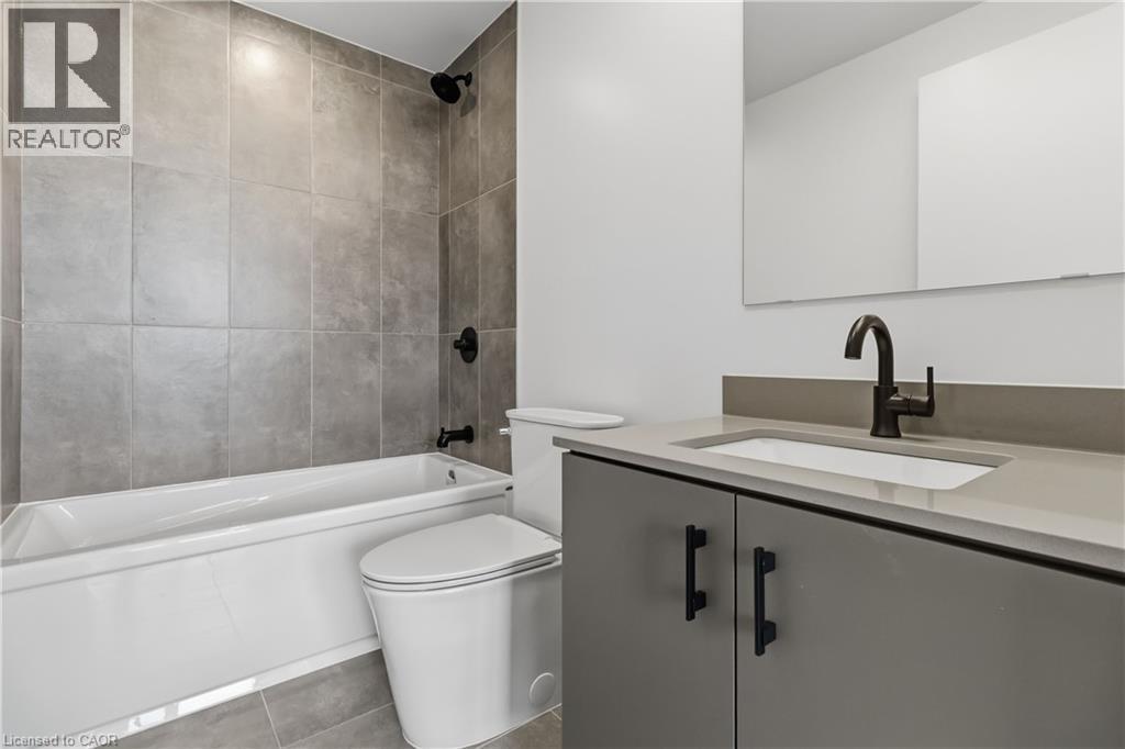 Bathroom featuring a bathtub with subway tile surround, a modern toilet, and a vanity with an integrated sink and dark hardware - 4878 Powers Common Unit# 224, Burlington, ON - Indoor Photo Showing Bathroom