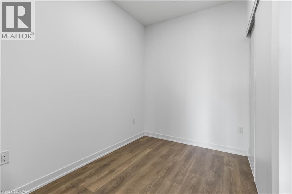 This room features light-colored walls, wood-style flooring, and a sliding door - 4878 Powers Common Unit# 224, Burlington, ON - Indoor Photo Showing Other Room